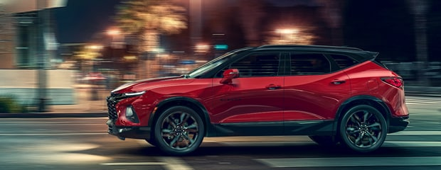 Red 2025 Chevrolet Blazer SUV driving on a city street with motion blur.
