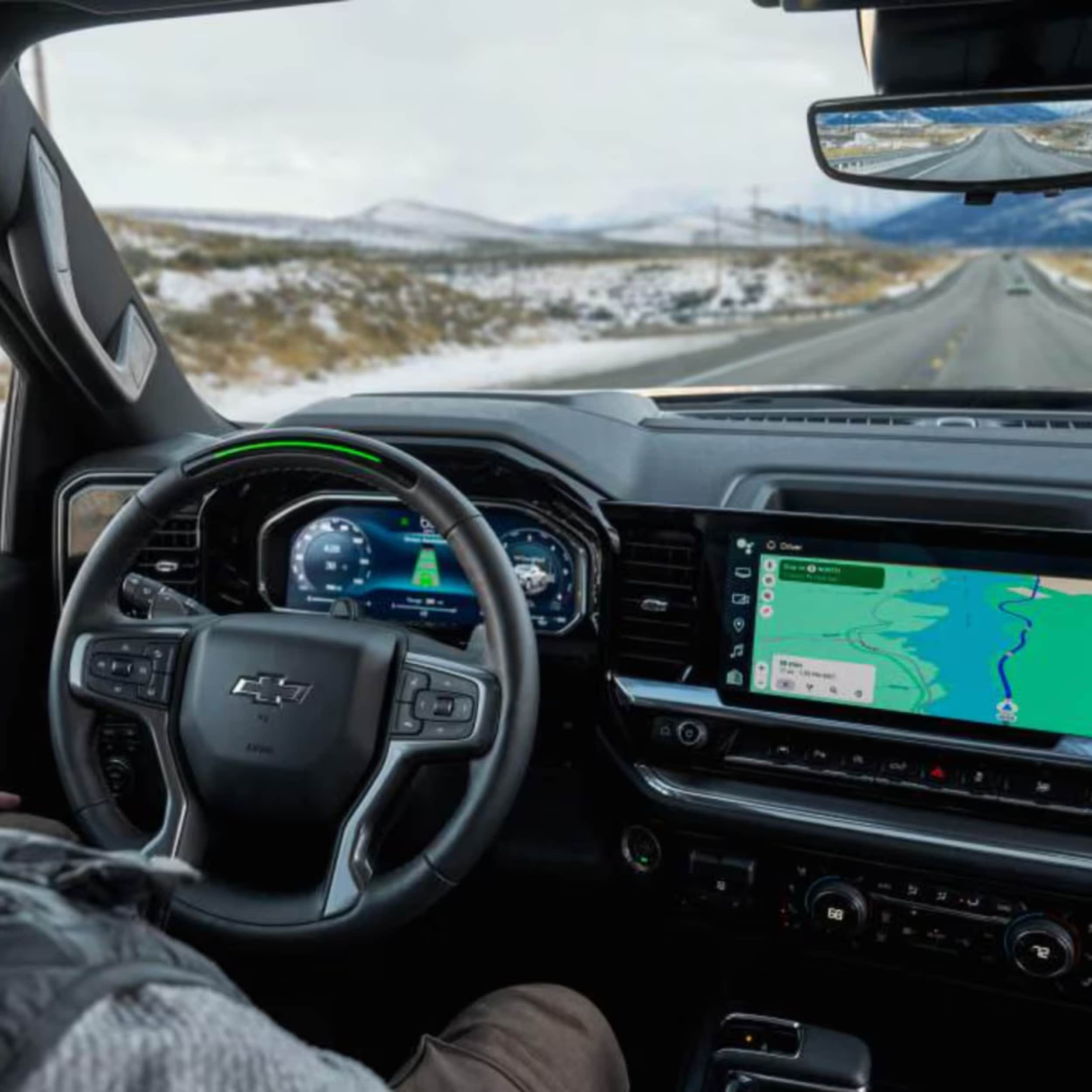 Car interior showing a black steering wheel with a gold Chevy logo, digital gauge cluster, and large infotainment touchscreen.