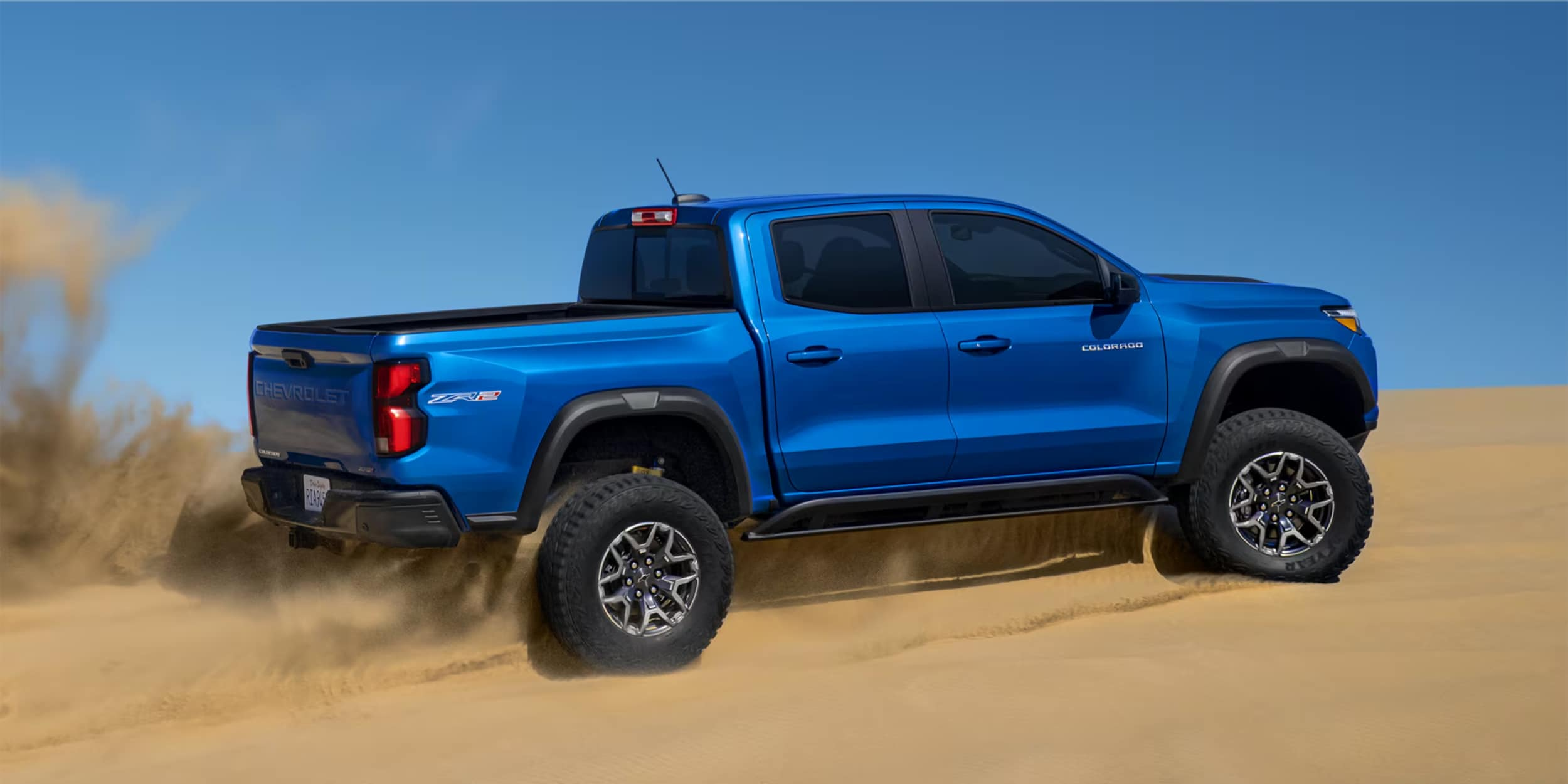 2024 Chevy Colorado is of blue color parked on the sandy area.