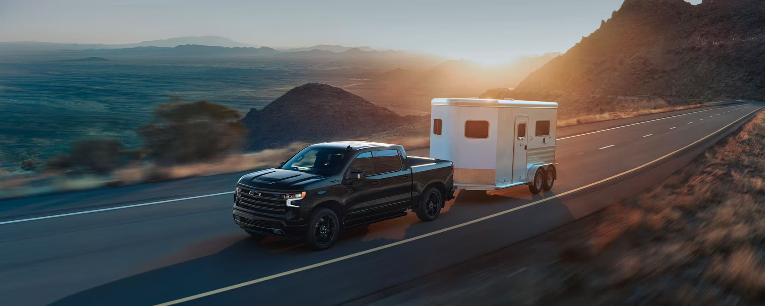 Green Chevrolet Silverado pickup truck is running on the road with sunset view in the background.