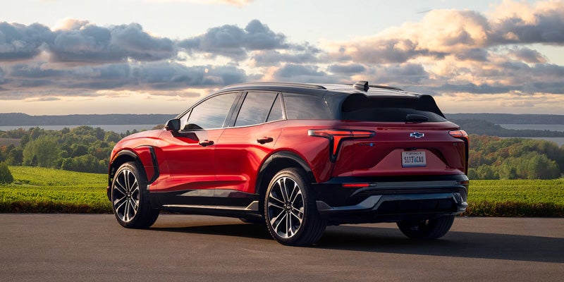 Red Chevrolet SUV parked on a scenic road overlooking a countryside landscape at sunset.