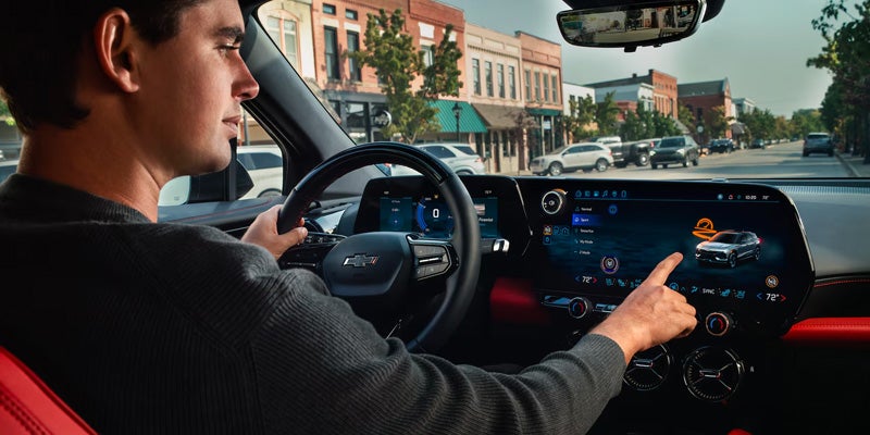 Driver using the touchscreen infotainment system inside a Chevrolet vehicle while driving through a small town.