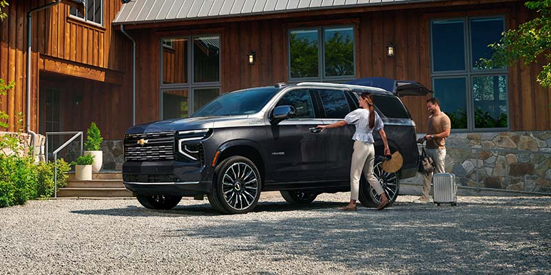 A dark-colored SUV parked on a gravel driveway in front of a wooden house