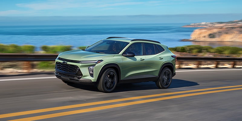 A light-colored SUV driving on a paved road along a coastline