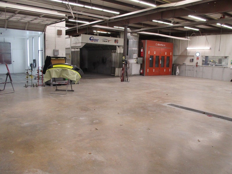 An empty auto body shop featuring a large red paint booth, a repair bay, and a car bumper on a stand.