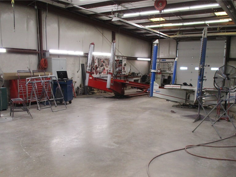 An empty auto body shop with red and white car alignment racks, toolboxes, and a creeper.